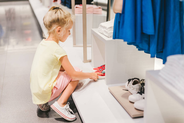 vista lateral de adorable niño pequeño elegir zapatos en la tienda
  - Foto, imagen