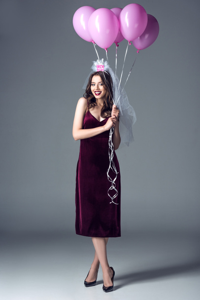 happy future bride in veil for bachelorette party holding bunch of pink air balloons on grey - 写真・画像