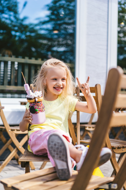 selective focus of happy adorable child doing rock gesture and holding delicious dessert in cafe  - Foto, Imagen