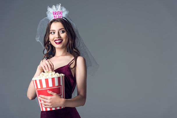 beautiful future bride in veil for bachelorette party eating popcorn isolated on grey - 写真・画像