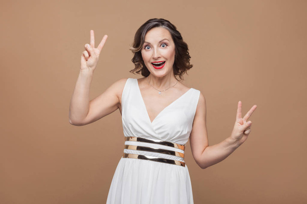 funny middle aged beautiful woman showing peace signs on brown background   - Photo, Image
