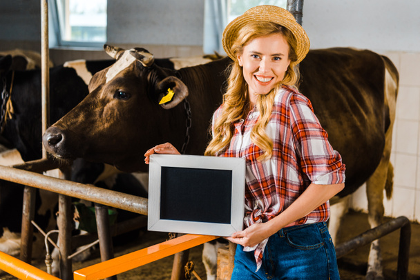 attractive farmer in straw hat showing blackboard in stable - Photo, Image