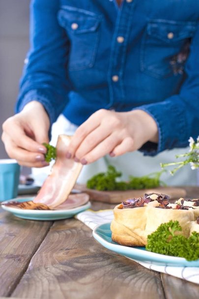 A girl in jeans clothes prepares a lunch of bacon and dough, with fresh herbs. Brown wooden background. Kramic dishes of blue cet. Free space for text - Foto, immagini