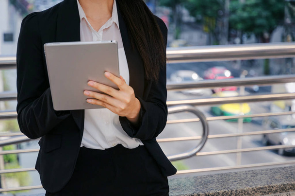 midsection young asian business woman wearing modern black suit playing social network with mobile tablet in building city background, network technology, internet, lifestyle and digital media concept - Φωτογραφία, εικόνα