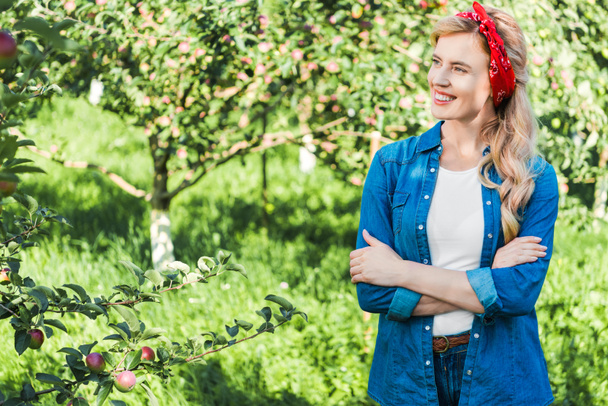 mosolygó vonzó farmer állandó apple kertben keresztezett karokkal - Fotó, kép