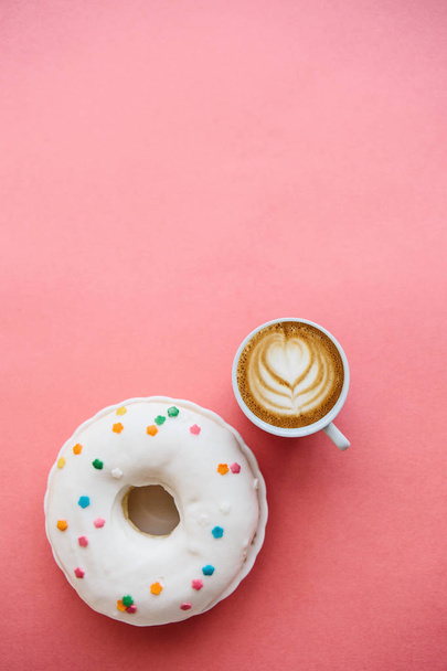 Donut ao lado de uma xícara de café perfumado ou cappuccino em um fundo vermelho. Acima do espaço para texto
 - Foto, Imagem