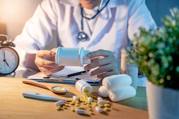 Male Asian doctor holding pill bottle. Doctor working with medicine paperwork clipboard on the desk in hospital clinic. Medical treatment and health care diagnostic concepts. - Photo, Image