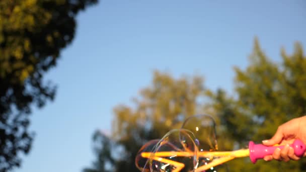 Menina soprando grandes bolhas no parque da cidade contra o céu azul. Close-up. Movimento lento
 - Filmagem, Vídeo