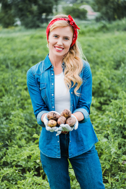 hymyilevä houkutteleva viljelijä, jolla on kypsiä perunoita maatilalla
 - Valokuva, kuva