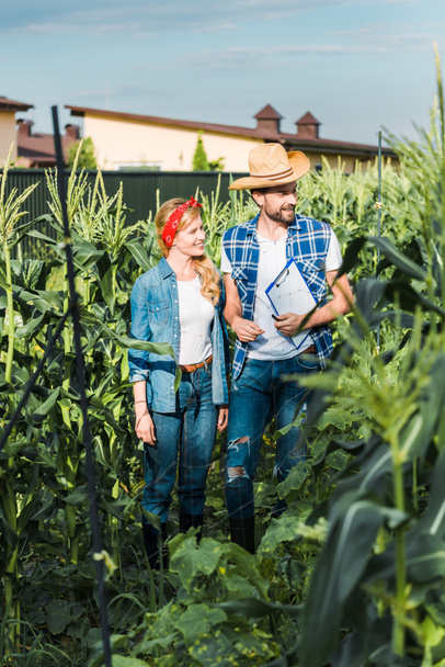 couple of smiling farmers checking harvest with clipboard in field at farm  - Фото, изображение