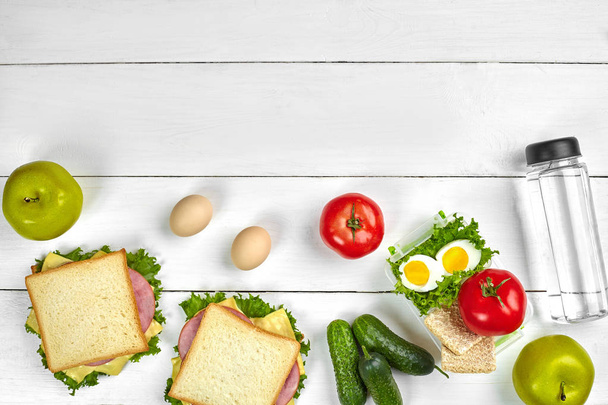 Lunch. Broodjes en verse groenten, fles water en groene appel op houten tafel. Gezond eten concept. Bovenaanzicht - Foto, afbeelding