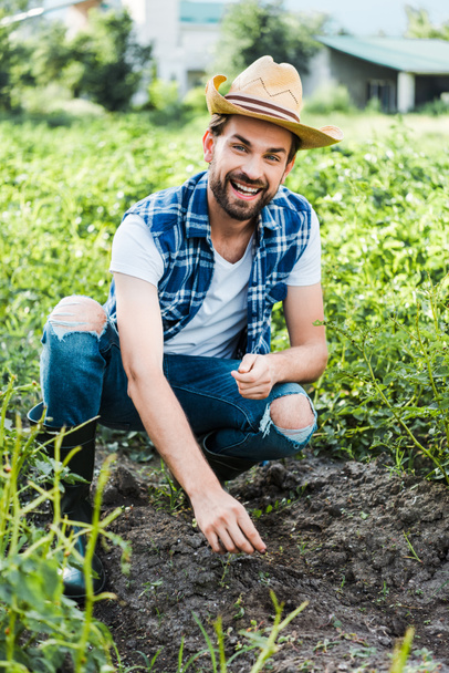 Ευτυχισμένος όμορφος αγρότης φυτεύοντας σπόρους κάρδαμο στον τομέα στο αγρόκτημα - Φωτογραφία, εικόνα