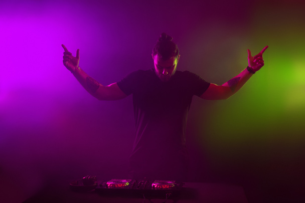 DJ au travail mélangeant le son sur ses ponts lors d'une fête ou d'une boîte de nuit avec un fond lumineux de fumée coloré
 - Photo, image
