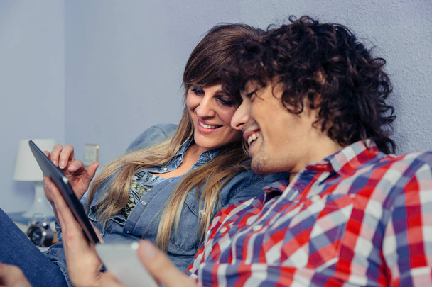 Primer plano de pareja joven enamorada mirando tableta electrónica y riendo mientras descansa sobre una cama. El tiempo libre en el hogar concepto
. - Foto, imagen
