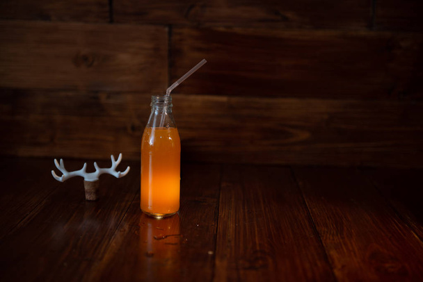 ένα vintage μπουκάλι φρεσκοστυμμένο χυμό σε ένα ξύλινο υπόβαθρο και ένα λαμπερό εμπορικό και. Κοντά σε φελλού κρασιού διακοσμημένο με κέρατα ελαφιών - Φωτογραφία, εικόνα