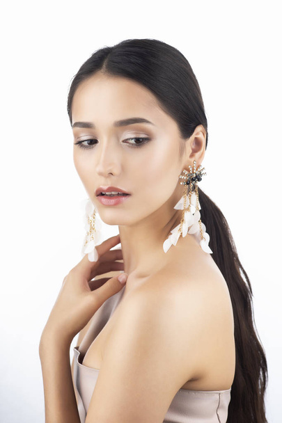 Beauty portrait of a beautiful smiling brunette girl model with bare shoulders and brown eyes wearing earrings imitation jewelry isolated on white background. Commercial design. Copy space. - Zdjęcie, obraz