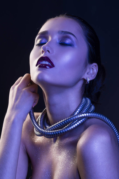 Beautiful brunette girl with naked shoulders and dark red lips make-up, wears a metal shower spiral hose wrapped around her neck. Concept and advertising low key photo illuminated in blue. Copy space - Foto, immagini