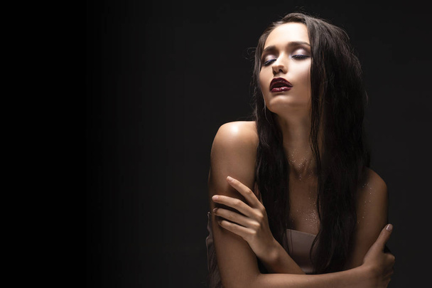 Beautiful sensual young brunette girl model with naked shoulders and dark red lips makeup on dark background. Commercial and advertising low key photo. Copy space - Фото, зображення