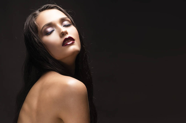 Linda sensual jovem morena modelo de menina com ombros nus e maquiagem lábios vermelhos escuros no fundo escuro. Foto comercial e publicidade low key. Espaço de cópia
 - Foto, Imagem