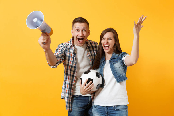 Young happy cheerful couple supporter, woman man, football fans cheer up support team, holding megaphone, soccer ball isolated on yellow background. Sport, family leisure, people lifestyle concept - Photo, Image