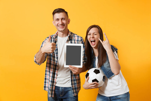 若い楽しいカップル サポーター、女性男性ファンを応援サポート チーム、サッカー空画面サッカー ボールが黄色の背景に分離された空白の黒とタブレット pc コンピューターを保持しています。スポーツ、家族のライフ スタイル - 写真・画像