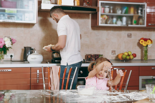 少女の子供は、パパのテーブルで、キッチンで料理しながら小麦粉を果たしています。幸せ家族のお父さん、週末の朝自宅で料理子娘。父の日の休日。親、小児コンセプト - 写真・画像