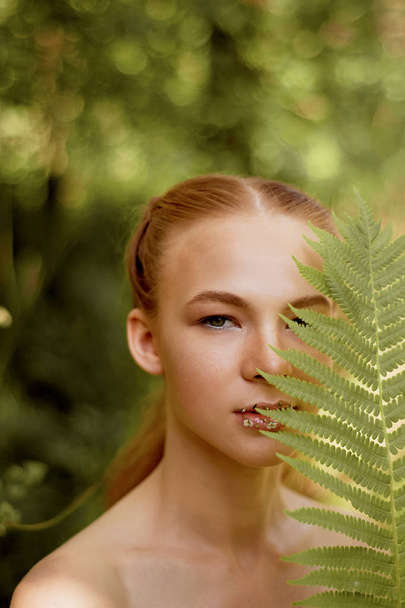 Portrait of a red-haired girl with long hair. The hair gathered in a ponytail. Near the face fern. Artistic portrait. Child of nature.The proximity to the naturalness and naturalness - Foto, Imagem