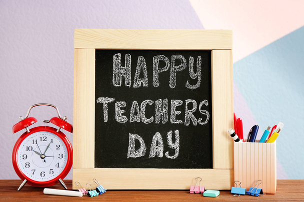 Little blackboard with inscription HAPPY TEACHER'S DAY, alarm clock and stationery on table - Фото, изображение