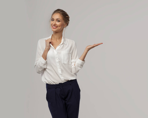 A beautiful business woman in a white classic office shirt demonstrates something on her hand with an open palm and smiles. Concept of business presentation - Fotó, kép