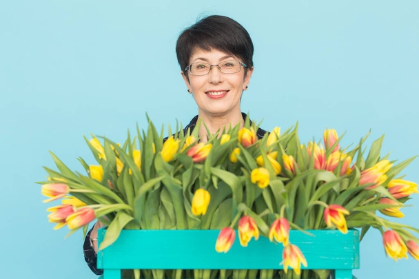 Mujer caucásica de mediana edad con un gran manojo de tulipanes sobre fondo azul
 - Foto, imagen