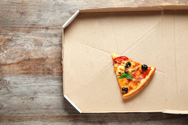 Last slice of tasty pizza in cardboard box on wooden table, top view - Zdjęcie, obraz