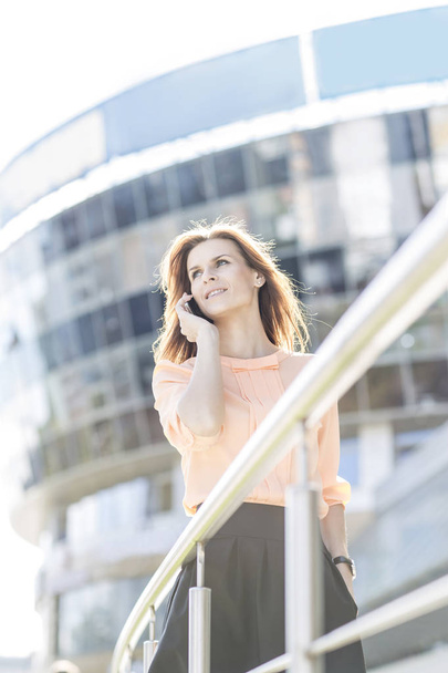 successful business woman talking on smartphone in front of a big modern office building - 写真・画像