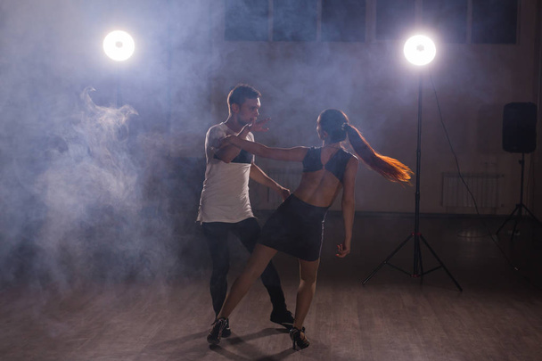 Skillful dancers performing in the dark room under the concert light and smoke. Sensual couple performing an artistic and emotional contemporary dance - Photo, Image