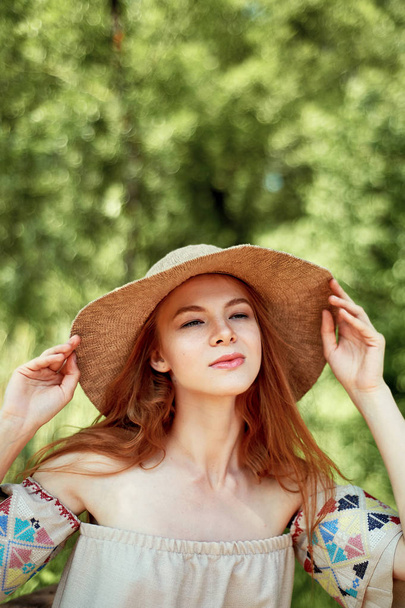 A sophisticated red-haired girl in a simple linen dress, in a light wide-brimmed hat.Model look. Natural beauty. Artistic portrait. Keeps the brim - Fotoğraf, Görsel