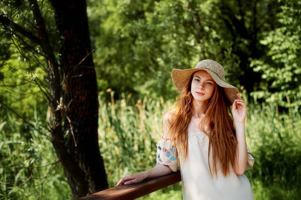 A sophisticated red-haired girl in a simple linen dress, in a light wide-brimmed hat.Model look. Natural beauty. Artistic portrait - Foto, immagini