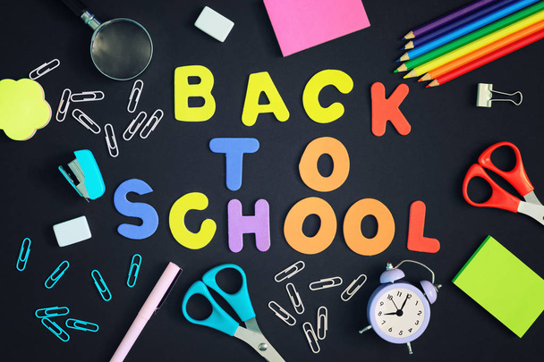 A fekete háttér vannak gémkapcsot, egy notebook, egy ébresztőóra és iskolai kellékek. A közepén a felirat, színes betűkkel vissza az iskolába. Fényes fotó. - Fotó, kép