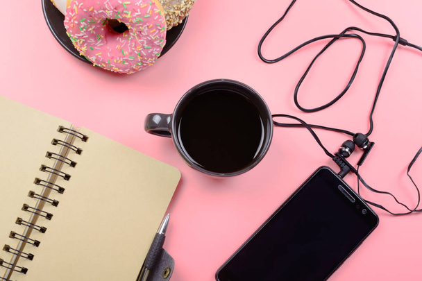 Notizblock auf Federn, eine Tasse Kaffee und ein Telefon mit Kopfhörer auf leuchtend rosa Hintergrund. Platz für Text. schönes helles Layout. - Foto, Bild