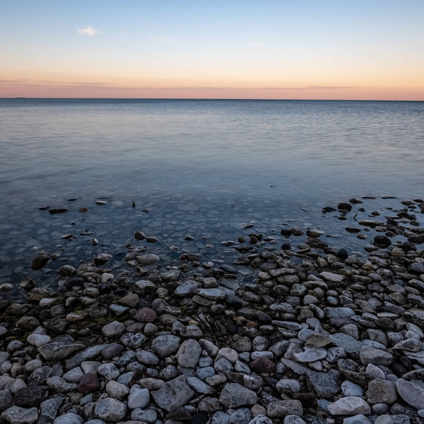 dramático amanecer sobre el mar báltico con playa rocosa y árboles en la orilla. Disparo de larga exposición. Estonia, isla de Hiiumaa
 - Foto, Imagen