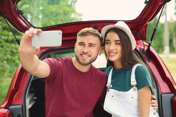 Beautiful young couple taking selfie in car trunk - Фото, изображение