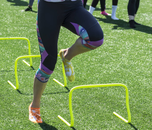 Ένα κομμάτι αθλητής εκτελεί ταχύτητα και ευκινησία ασκήσεις πάνω από το κίτρινο μίνι εμπόδια φορώντας κάλτσες διαφορετικό χρώμα, ένα πορτοκάλι και το άλλο κίτρινο και όχι παπούτσια. - Φωτογραφία, εικόνα