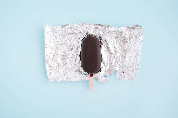 Karanlık çikolatalı dondurma, dondurma gümüş kağıt sarma yukarıdan üzerinde. Pastel mavi arka plan. Minimalist gıda Fotoğrafçılık. Boşaltmak - Fotoğraf, Görsel