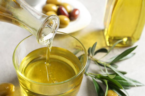 Pouring fresh olive oil into glass on table - Valokuva, kuva