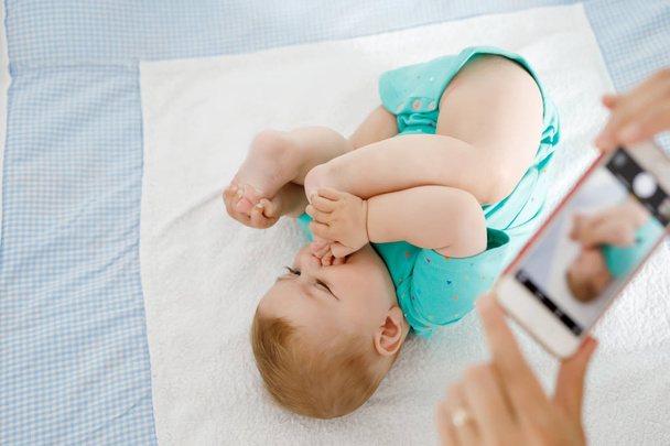Parent taking photo of a baby with smartphone. Adorable newborn child taking foot in mouth - Photo, Image