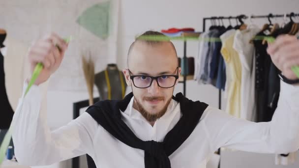 Portrait of a bearded tailor in glasses with making using the tape measure at atelier. Concept: Fashion designer, tailoring, produce clothes, slow motion - Záběry, video