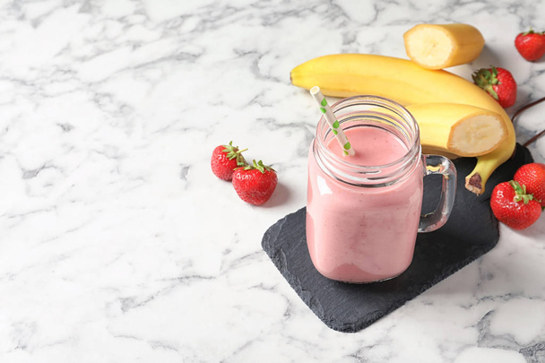 Mason jar with tasty strawberry smoothie on marble table - 写真・画像