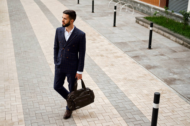 Привабливий бізнесмен, що йде по вулиці тримає сумку для подорожей
 - Фото, зображення