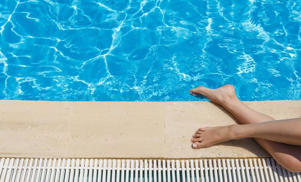 Jonge vrouw is zonnebaden bij een turkoois zwembad op een zonnige dag - Foto, afbeelding