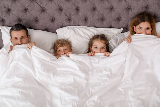 Ζευγάρι με τα παιδιά που βρίσκονται κάτω από την κουβέρτα στο κρεβάτι. Ευτυχισμένη οικογένεια - Φωτογραφία, εικόνα