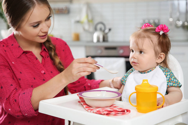 Mother feeding her little baby with healthy food in kitchen - Foto, imagen