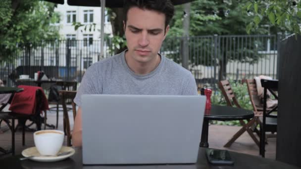 Gähnend müder Mann benutzt Laptop auf Caféterrasse - Filmmaterial, Video